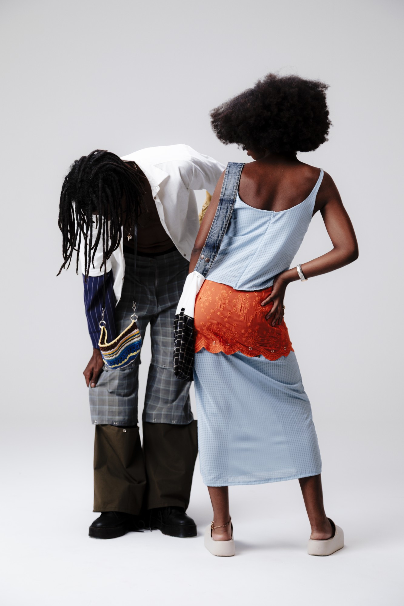 Dupla de modelos de costas: uma pessoa inclinada com a bolsa de crochê, outra com a bolsa de alça jeans